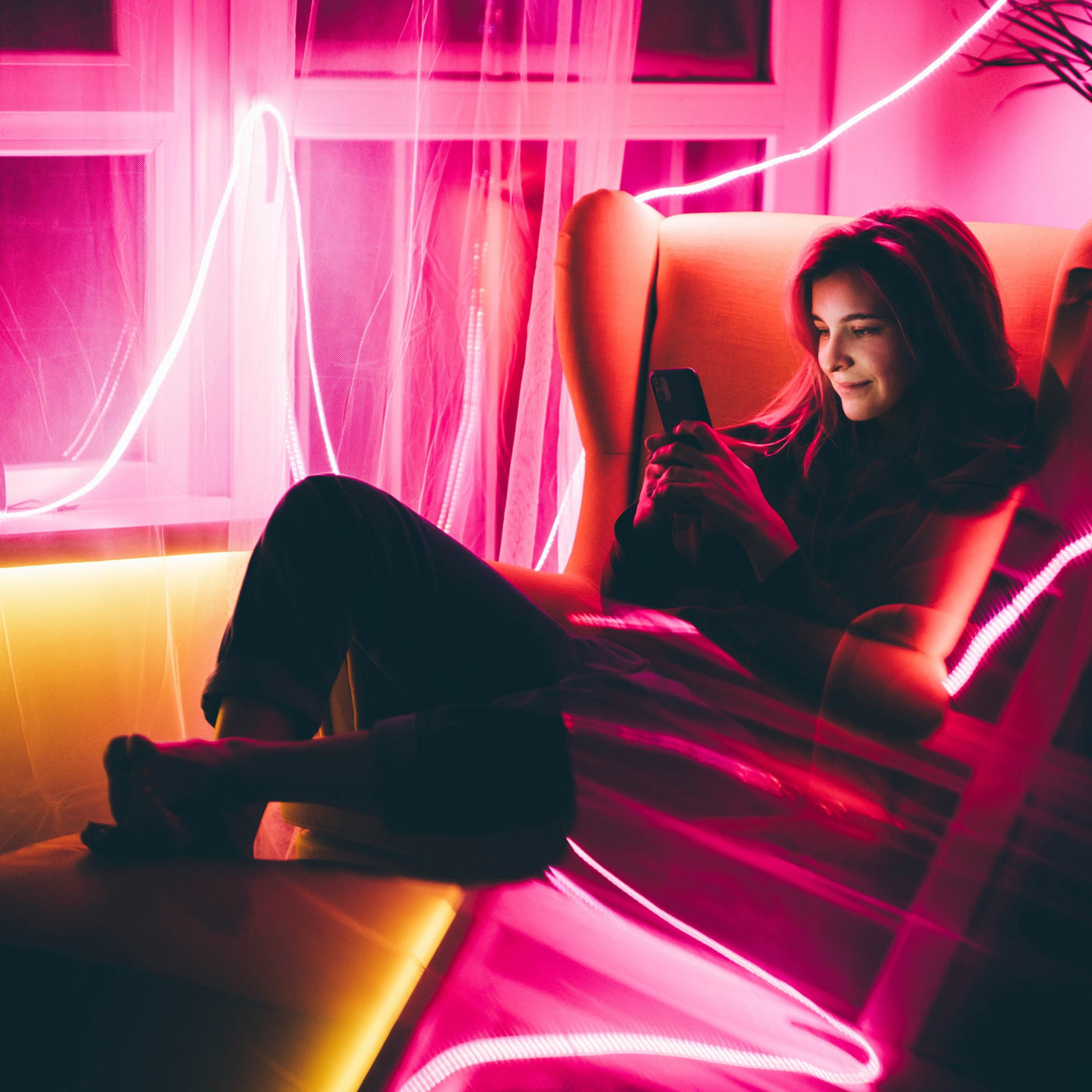 Young woman making video call with smart phone in living room with neon light at home .